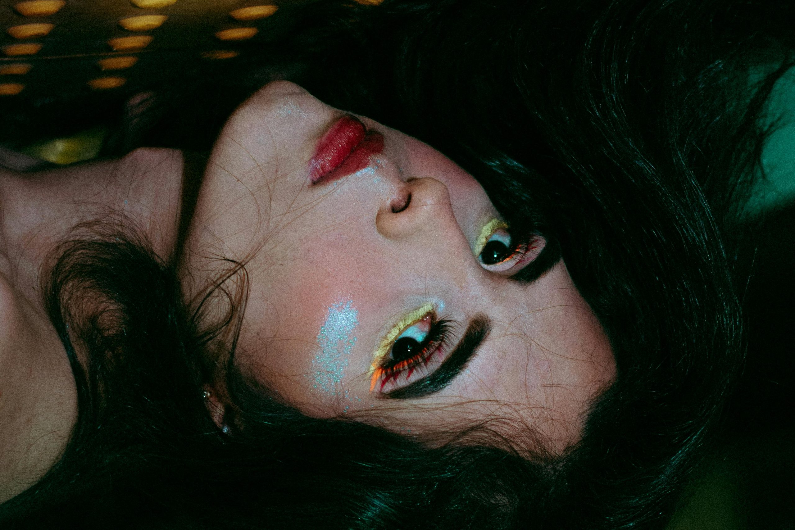 Intriguing portrait of a woman with vibrant eye makeup and red lips, creates a dramatic visual effect.